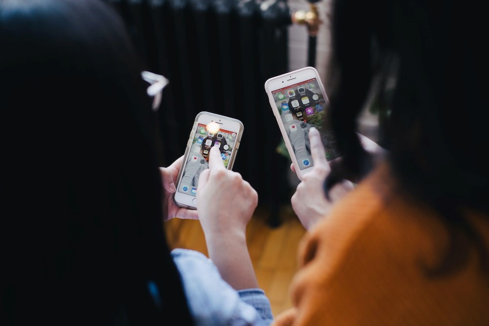 Two girl is pointing at their own mobile phone